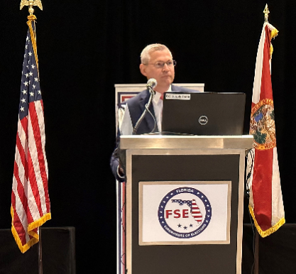 A photo of FSE President Ron Turner (Sarasota County SOE) speaking at a podium.
